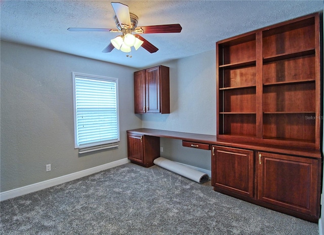 unfurnished office featuring a textured ceiling, baseboards, dark carpet, and built in desk