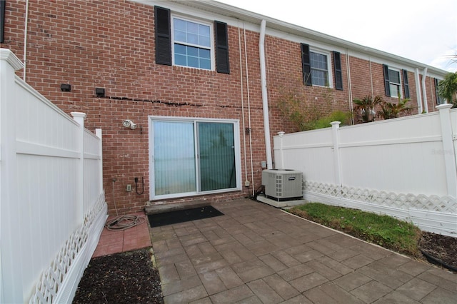 back of property featuring cooling unit, brick siding, fence, and a patio