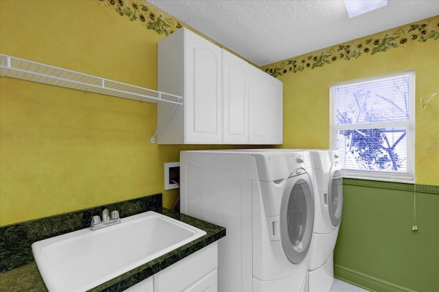 laundry room with washing machine and dryer, cabinet space, a sink, and a textured ceiling