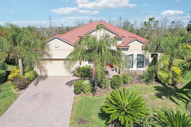 mediterranean / spanish-style home with stucco siding, a front lawn, decorative driveway, an attached garage, and a tiled roof