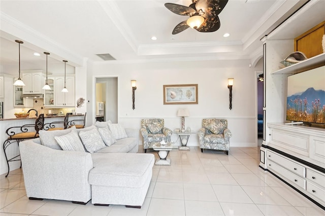 living room with ceiling fan, a raised ceiling, light tile patterned flooring, and ornamental molding