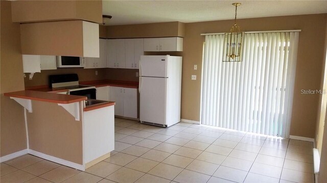 kitchen with white appliances, light tile patterned flooring, a peninsula, and white cabinetry