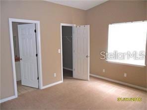 unfurnished bedroom featuring carpet floors, baseboards, a walk in closet, and a closet