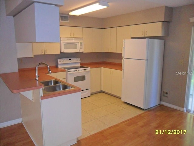 kitchen with visible vents, light wood-style flooring, a sink, white appliances, and a peninsula