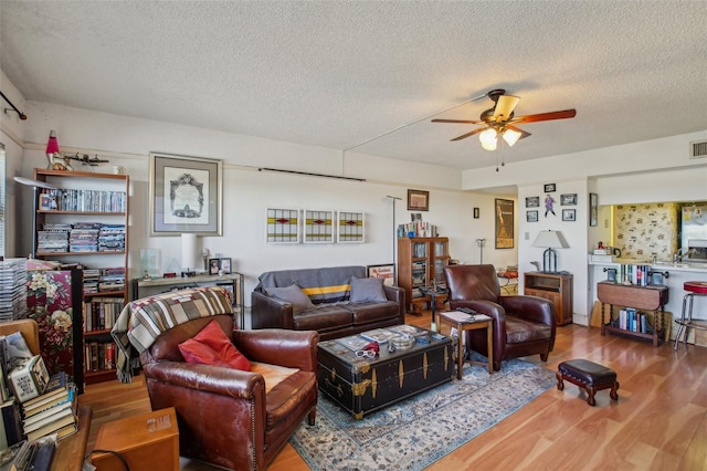 living area featuring ceiling fan, visible vents, a textured ceiling, and wood finished floors