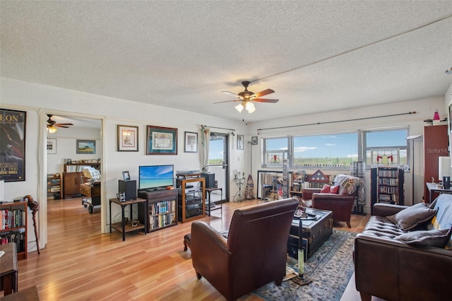 living room with a textured ceiling, a ceiling fan, and light wood finished floors