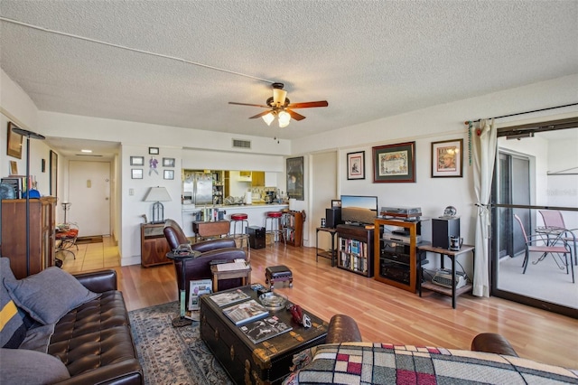 living room featuring visible vents, a textured ceiling, a ceiling fan, and wood finished floors