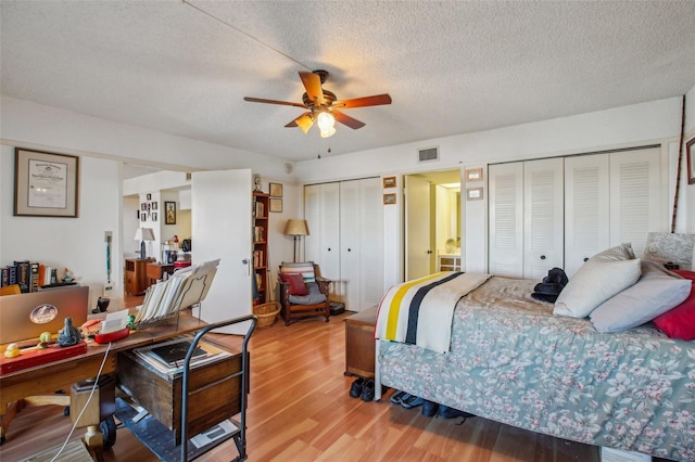 bedroom featuring visible vents, two closets, wood finished floors, a textured ceiling, and a ceiling fan