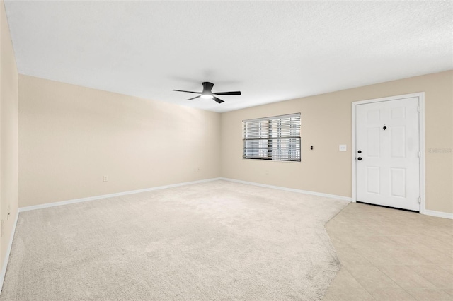 spare room featuring a textured ceiling, a ceiling fan, baseboards, and light carpet