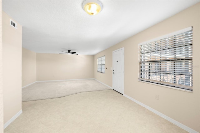 interior space with visible vents, a ceiling fan, a textured ceiling, baseboards, and light colored carpet