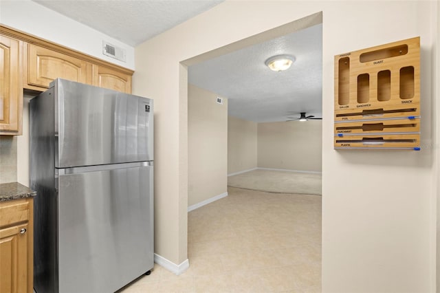 kitchen with visible vents, dark stone countertops, a textured ceiling, freestanding refrigerator, and baseboards