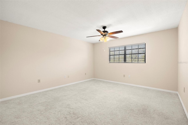 spare room with light colored carpet, a textured ceiling, baseboards, and a ceiling fan