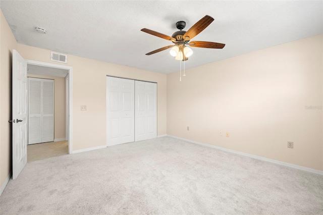 unfurnished bedroom featuring visible vents, baseboards, light carpet, a closet, and a ceiling fan