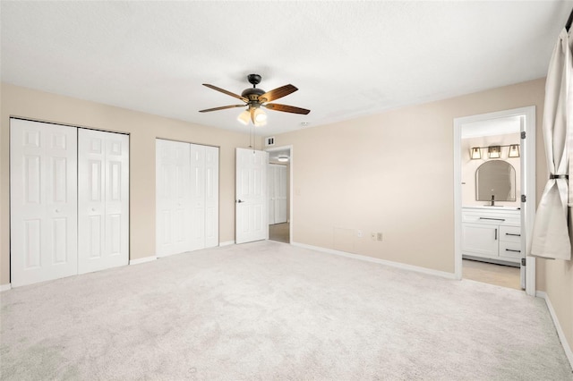 unfurnished bedroom with light carpet, baseboards, ensuite bath, and multiple closets