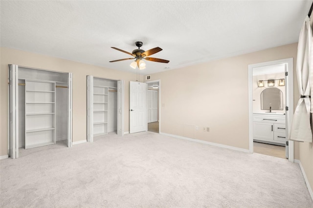 unfurnished bedroom featuring light colored carpet, baseboards, two closets, and a textured ceiling