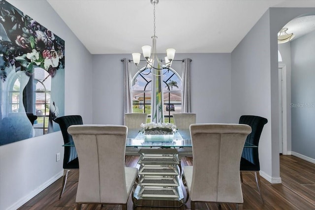 dining space featuring a chandelier, arched walkways, dark wood finished floors, and baseboards