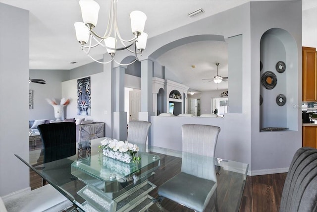 dining space with arched walkways, ceiling fan with notable chandelier, wood finished floors, visible vents, and baseboards