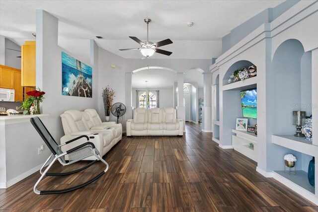 living area featuring arched walkways, ceiling fan with notable chandelier, wood finished floors, baseboards, and decorative columns