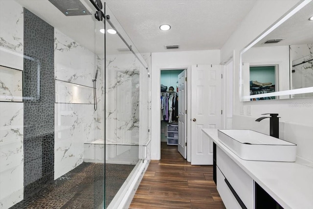 full bathroom featuring a walk in closet, visible vents, a marble finish shower, and wood finished floors