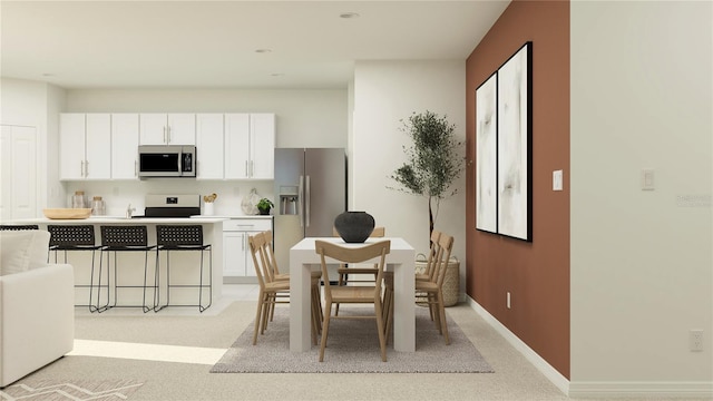 kitchen with a breakfast bar area, stainless steel appliances, light colored carpet, white cabinetry, and baseboards