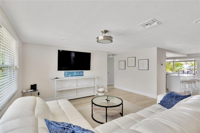 living room featuring baseboards, light wood-style flooring, visible vents, and a textured ceiling