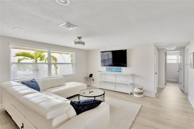 living room with a textured ceiling, baseboards, visible vents, and light wood-style floors