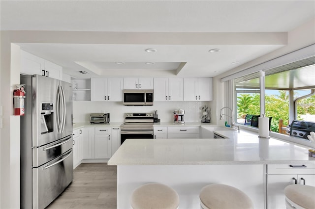 kitchen with open shelves, stainless steel appliances, a raised ceiling, a sink, and a peninsula