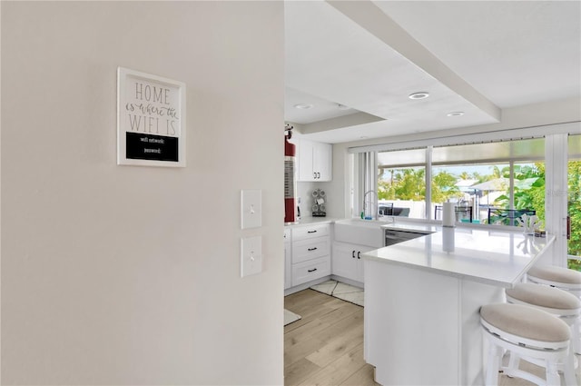 kitchen with a kitchen breakfast bar, a peninsula, a sink, light countertops, and stainless steel dishwasher