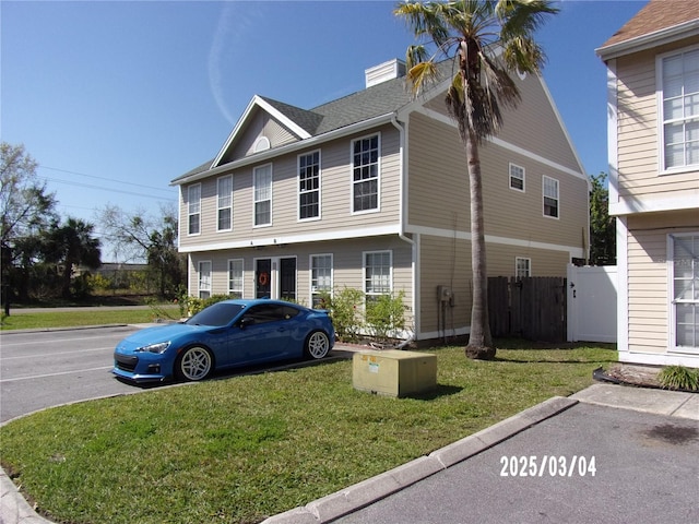 colonial-style house with fence, a chimney, and a front lawn