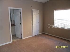 unfurnished bedroom with baseboards, carpet flooring, and ensuite bathroom