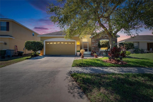 view of front of house with a yard, stucco siding, a garage, stone siding, and driveway