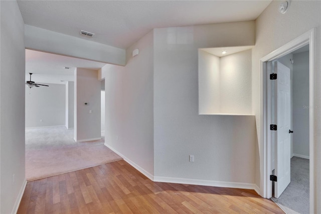 hallway with light wood-type flooring, visible vents, and baseboards