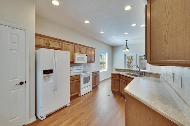 kitchen with white appliances, light wood finished floors, decorative backsplash, light countertops, and a sink