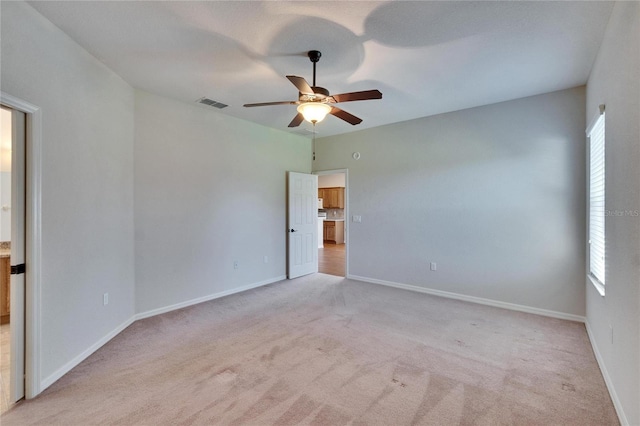 spare room featuring a ceiling fan, light colored carpet, visible vents, and baseboards