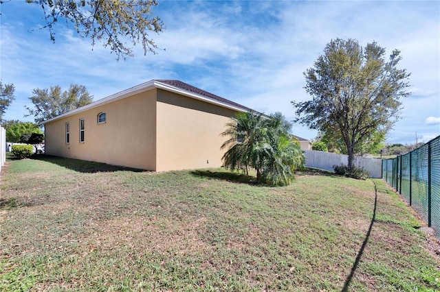 view of side of home featuring a lawn, fence, and stucco siding