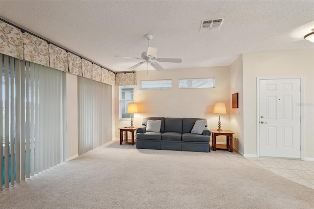 carpeted living area with a healthy amount of sunlight, baseboards, visible vents, ceiling fan, and a textured ceiling