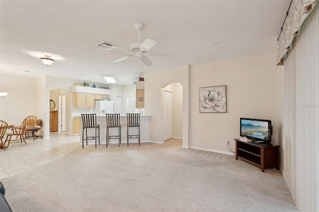 living area featuring visible vents, light carpet, arched walkways, light tile patterned floors, and ceiling fan