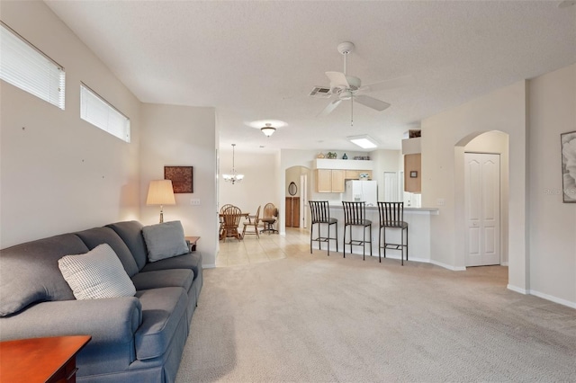 living area with baseboards, arched walkways, a textured ceiling, light carpet, and ceiling fan with notable chandelier