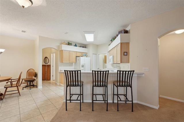 kitchen with white appliances, light tile patterned floors, a peninsula, arched walkways, and light brown cabinetry