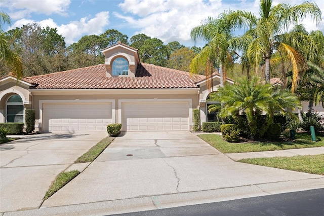 mediterranean / spanish house featuring an attached garage, a tile roof, concrete driveway, and stucco siding