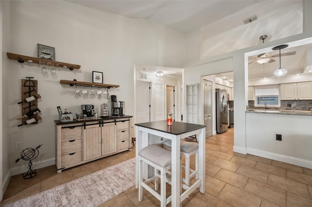 kitchen with dark countertops, visible vents, decorative backsplash, vaulted ceiling, and stainless steel fridge