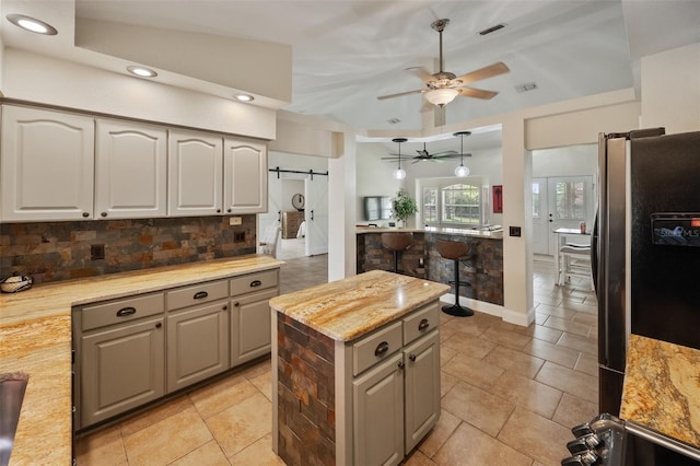 kitchen with a barn door, visible vents, gray cabinets, freestanding refrigerator, and decorative backsplash