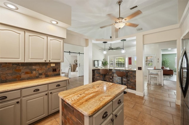 kitchen featuring visible vents, backsplash, a barn door, a ceiling fan, and a kitchen island