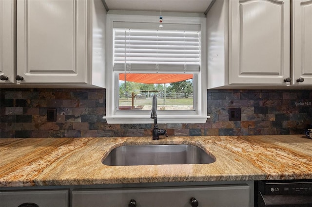 kitchen featuring backsplash, white cabinets, a sink, light stone countertops, and dishwasher