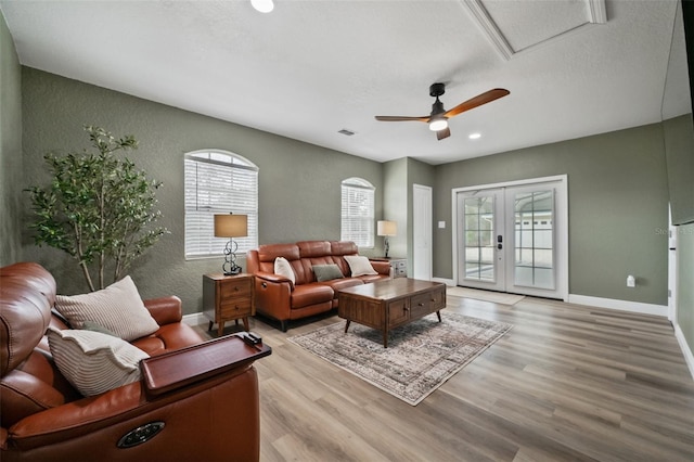 living area featuring a textured wall, light wood-style flooring, baseboards, and french doors