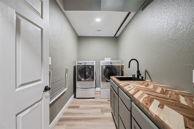 washroom with cabinet space, a textured wall, a sink, and independent washer and dryer