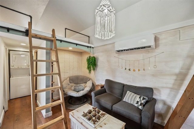 living room with a barn door, a notable chandelier, stacked washer / dryer, wood finished floors, and an AC wall unit