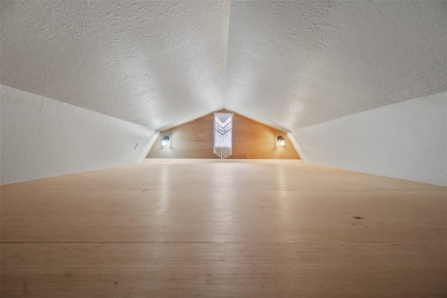 additional living space featuring vaulted ceiling, a textured ceiling, and a textured wall