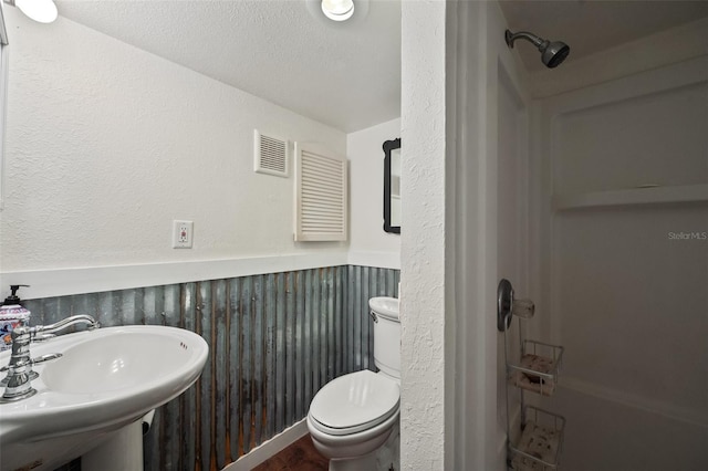 bathroom featuring visible vents, toilet, a wainscoted wall, a textured ceiling, and a sink