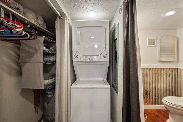 laundry room featuring a textured ceiling, visible vents, wood finished floors, and stacked washer and clothes dryer